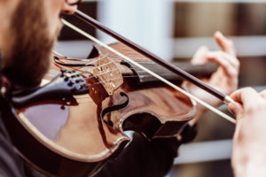 A close-up view captures the detailed artistry of a violinist in action, with a focus on the fingers deftly pressing the strings and the bow elegantly gliding across, creating a sense of the music's movement and the musician's skillful expression.