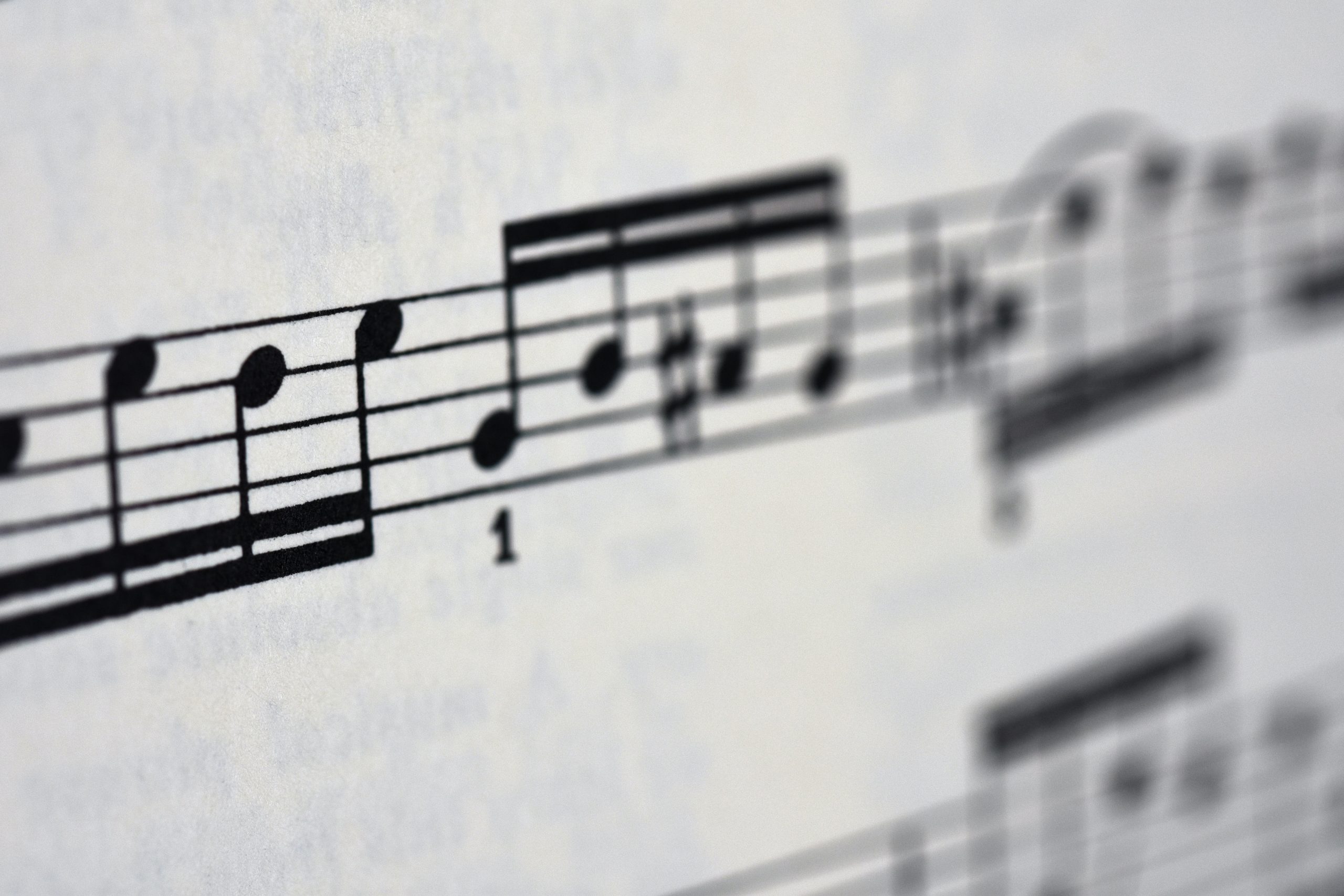 The image shows a close-up of a sheet of music with a focus on a section of the staff, where musical notes are printed. The shallow depth of field blurs the notes in the foreground and background, highlighting the crisp detail of the notes in the center. A number "1" is visible, possibly indicating a measure number or a finger positioning for playing an instrument.