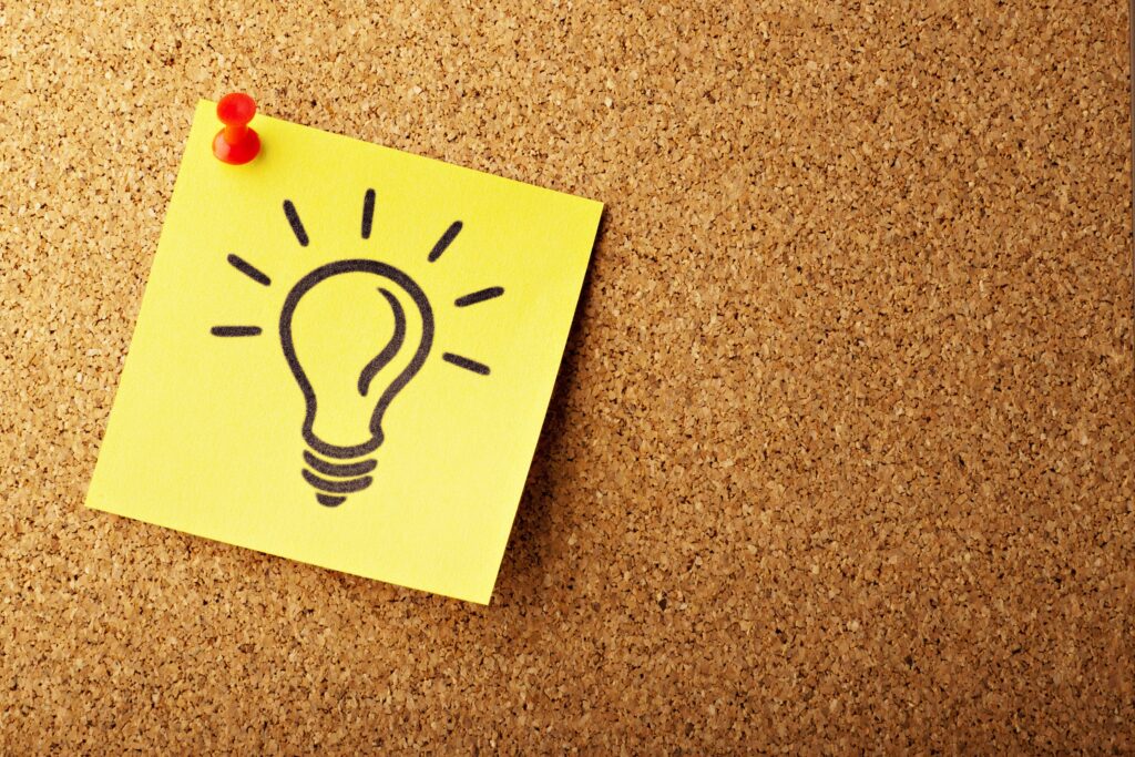 A yellow post-it note with a drawing of a light bulb is pinned to a cork board