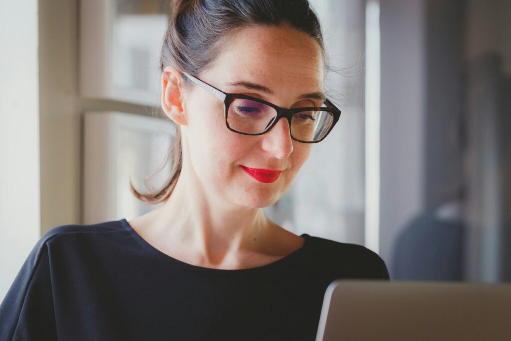 A woman with glasses is looking down at her laptop